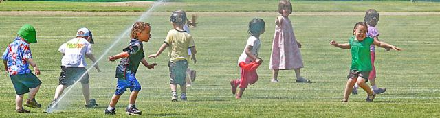 Kids frolic in lawn sprinkler shower - simple pleasure